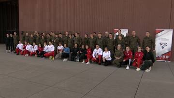 Grupa żołnierzy-sportowc&oacute;w, w tym kobiety i mężczyźni, w mundurach i strojach sportowych, pozuje do wsp&oacute;lnego zdjęcia na zewnątrz.