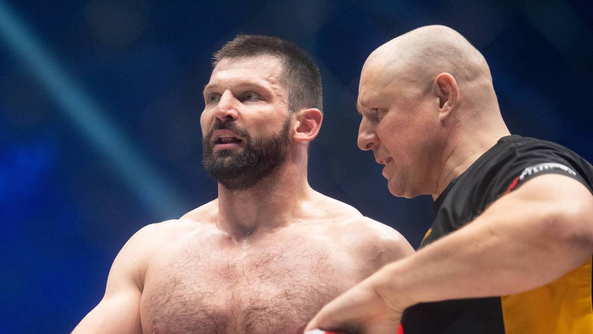 Zawodnik MMA w rękawicach bokserskich stoi obok trenera z czerwoną kurtką.