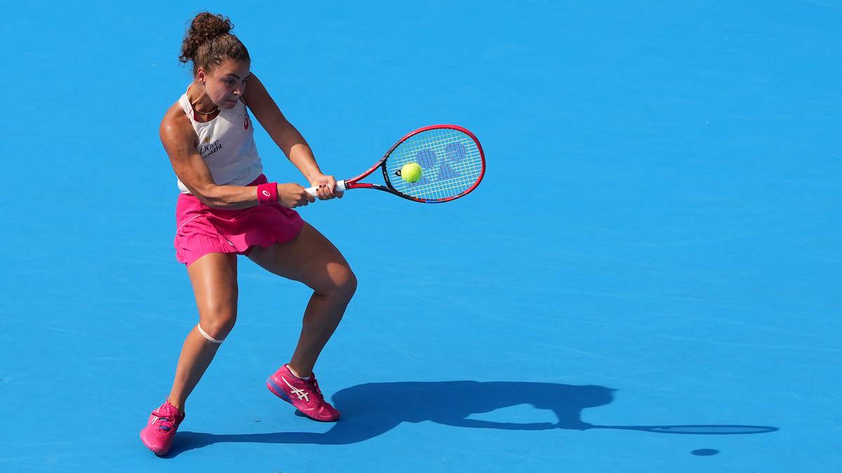 Kobieta grająca w tenisa, uderzająca piłkę rakietą na niebieskim tle.