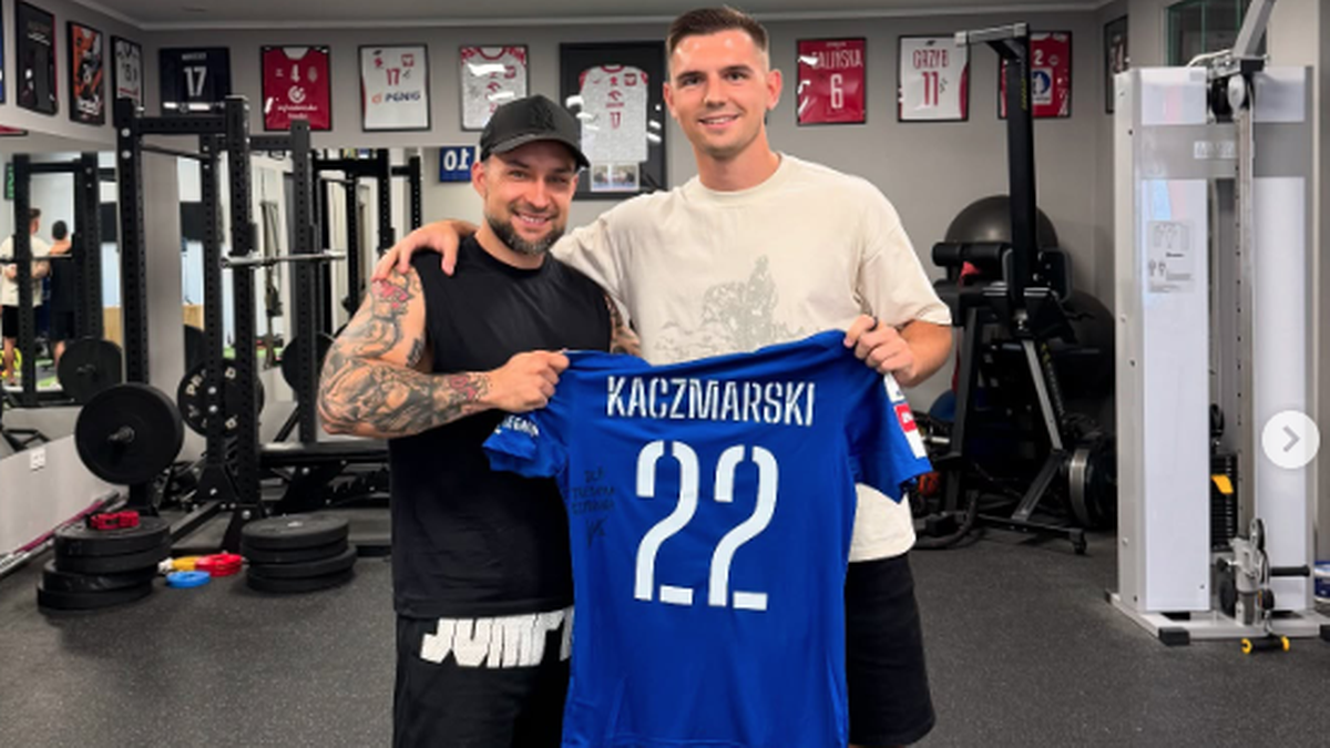 Dw&oacute;ch mężczyzn trzyma niebieską koszulkę z nazwiskiem KACZMARSKI i numerem 22.
