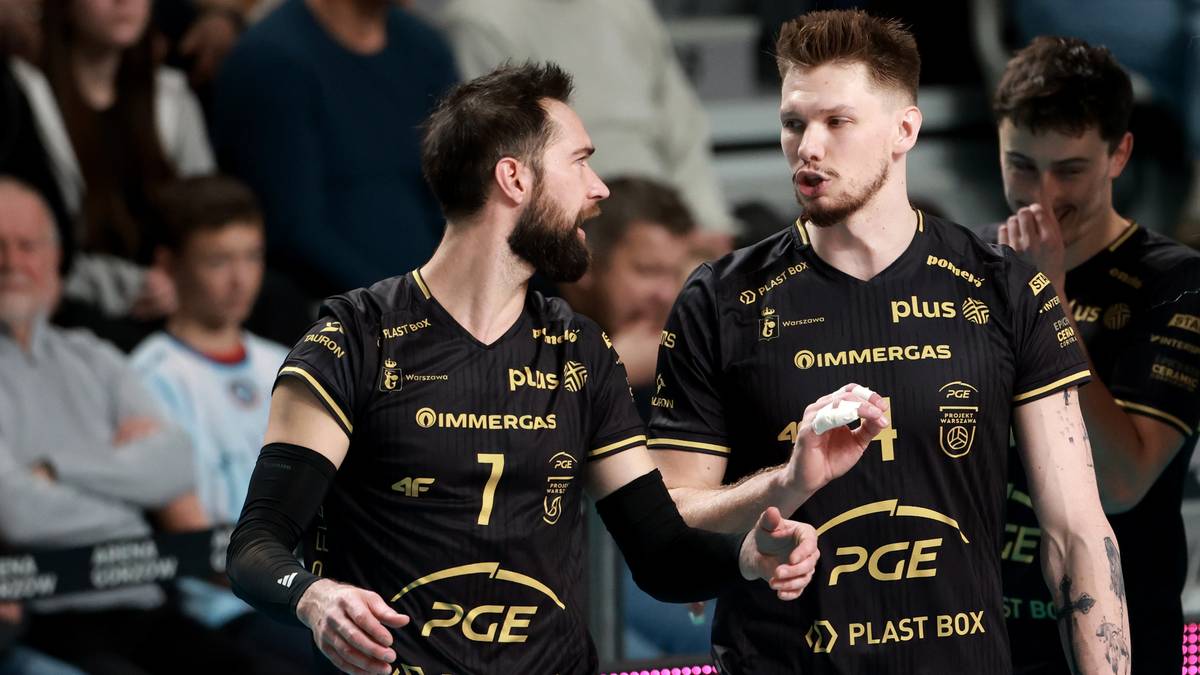 Dwóch siatkarzy w czarnych koszulkach z żółtymi akcentami rozmawia na boisku.