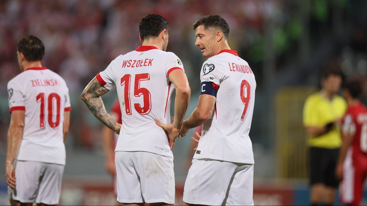 Trzech piłkarzy reprezentacji Polski w białych koszulkach z numerami 10, 15 i 9 rozmawia na boisku.