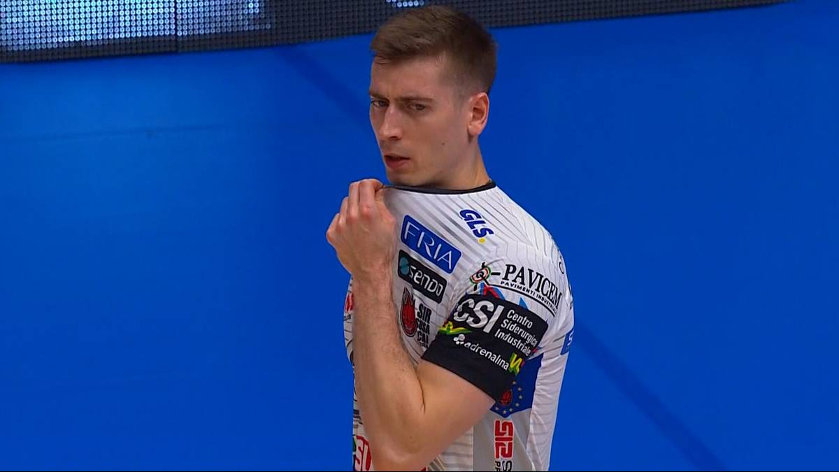 Siatkarz w koszulce sportowej z logotypami odwraca się w stronę kamery.