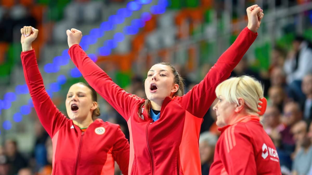 Trzy kobiety w czerwonych bluzach sportowych świętują zwycięstwo, trzymając ręce uniesione w górze.