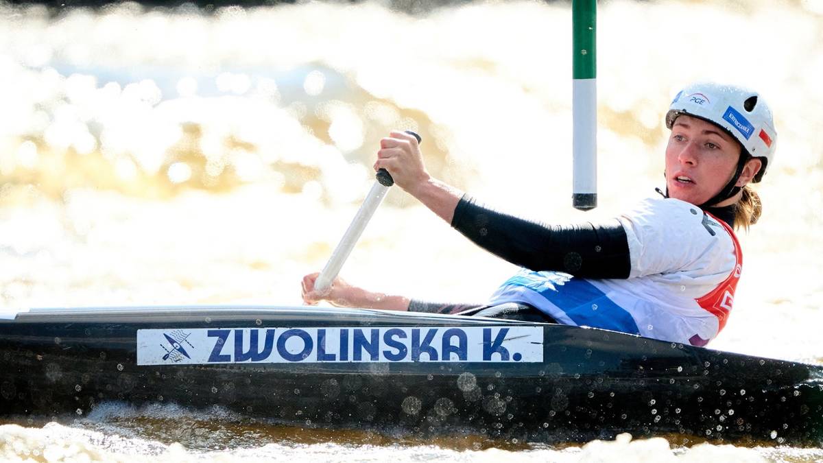 Kobieta w kasku siedzi w kajaku, wiosłując. Na kajaku widnieje napis "ZWOLINSKA K.".
