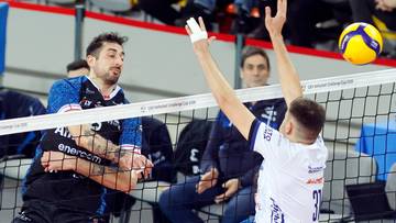 Siatkarze podczas meczu siatk&oacute;wki, jeden z nich wykonuje zagrywkę, a drugi blokuje.