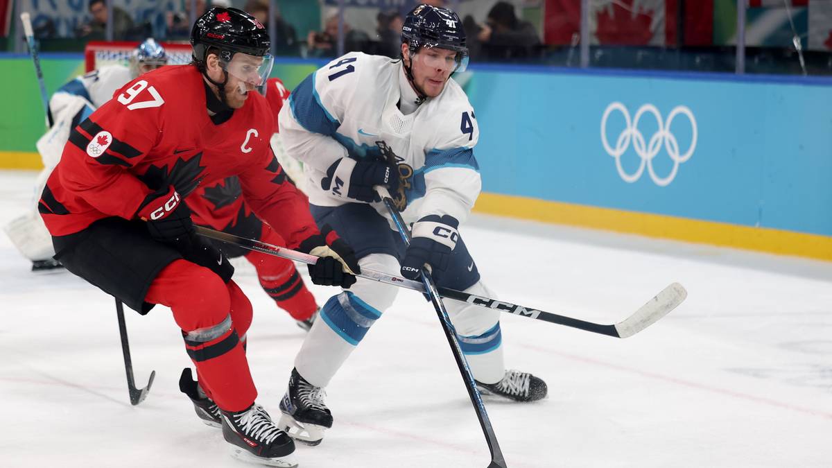 Dw&oacute;ch zawodnik&oacute;w hokeja na lodzie w akcji, jeden w czerwonym stroju Kanady, drugi w białym stroju przeciwnika, walczą o krążek.