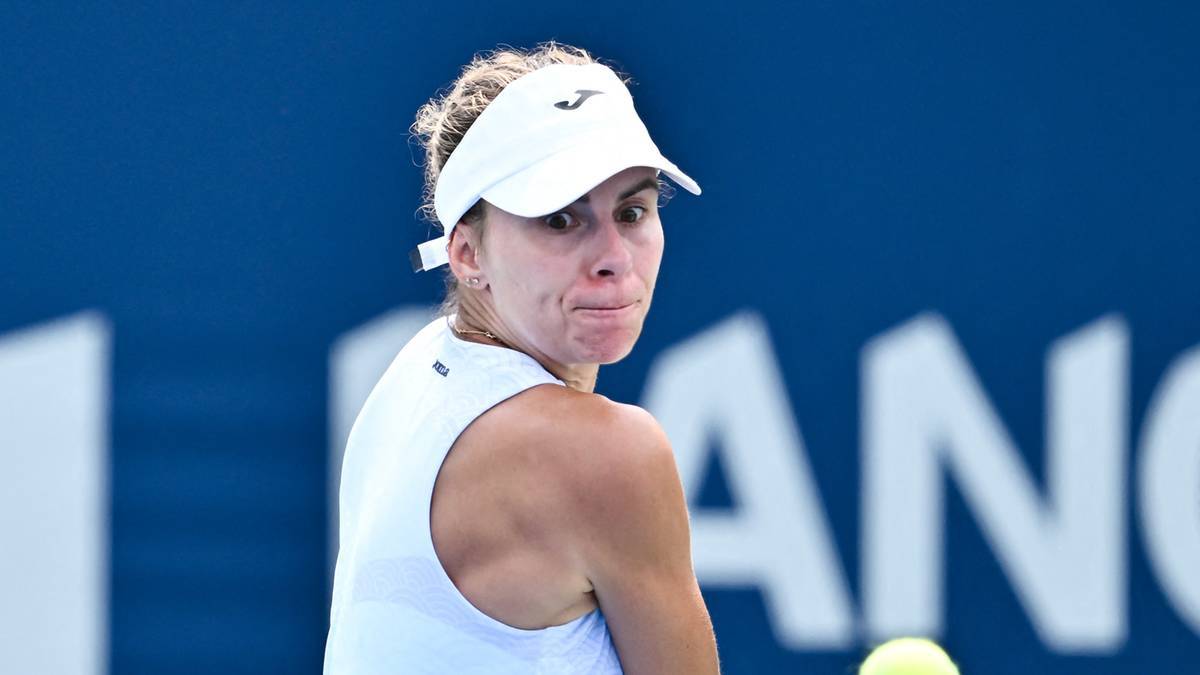 Tenisistka w białej czapce i białym topie, z determinacją na twarzy, obserwuje piłkę tenisową.