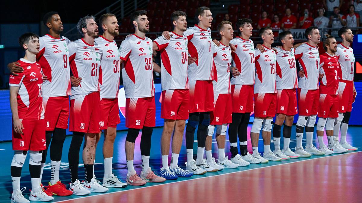 Drużyna siatkarzy reprezentacji Polski w białych i czerwonych strojach sportowych stoi w rzędzie na hali sportowej.