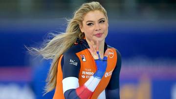 Łyżwiarka szybka w stroju reprezentacji Holandii unosi dłoń z dwoma palcami w geście "V".