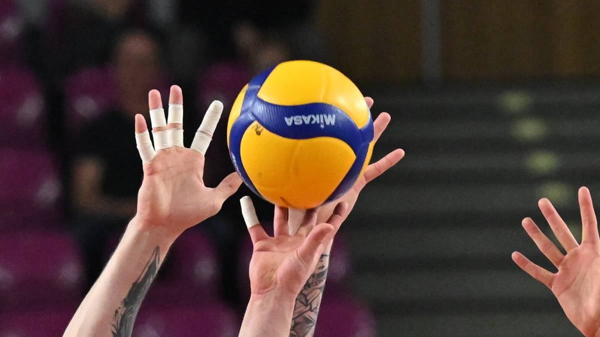 Siatkarze w akcji podczas meczu, jeden z nich blokuje piłkę.