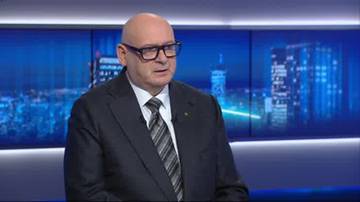 Mężczyzna w garniturze i okularach siedzi przed ekranami przedstawiającymi nocne miasto.