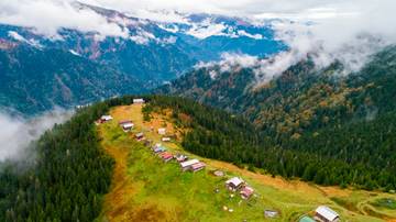 G&oacute;rzysty krajobraz z lasami, mgłą i niewielką osadą na zboczu.