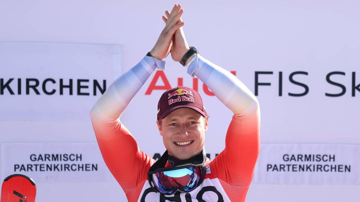 Narciarz alpejski świętujący zwycięstwo z uniesionymi rękami na podium.