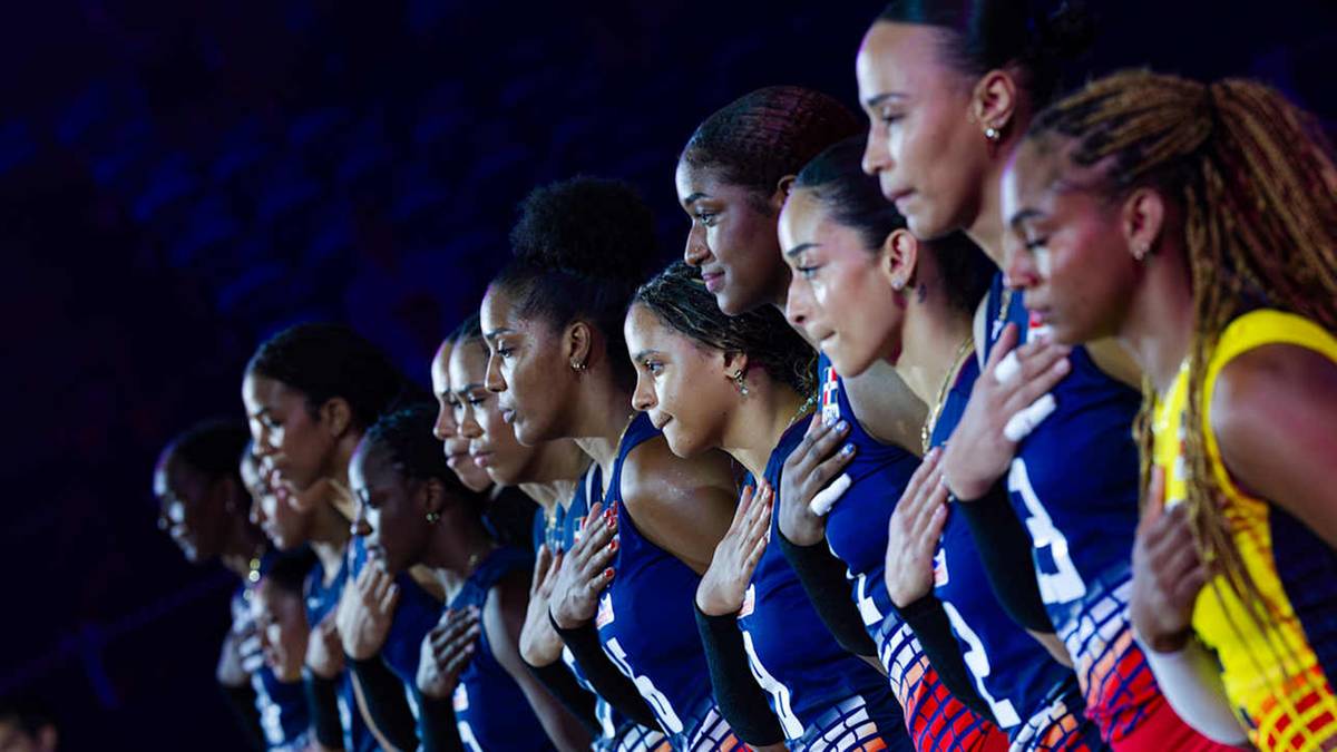 Grupa zawodniczek siatkówki na podium, trzymające dłonie na sercach.