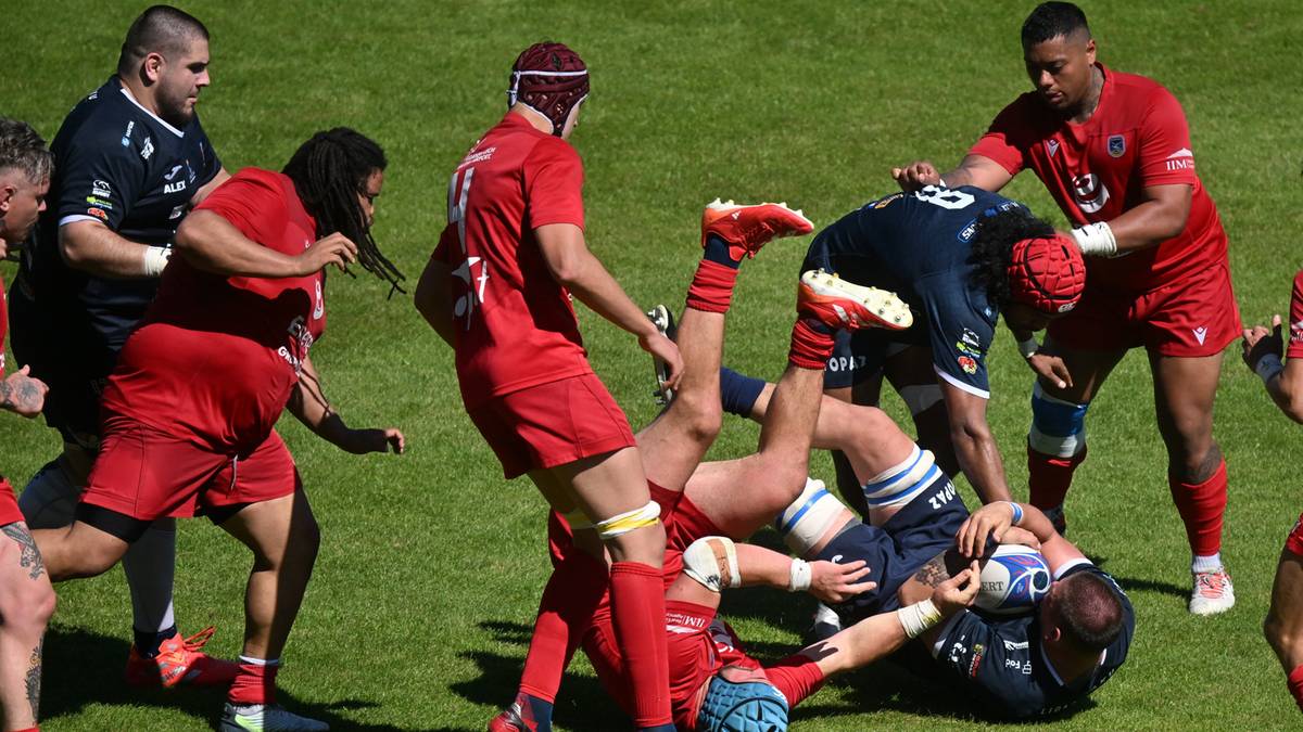 Zawodnicy drużyny rugby walczą o piłkę na boisku. Jeden z graczy leży na ziemi.
