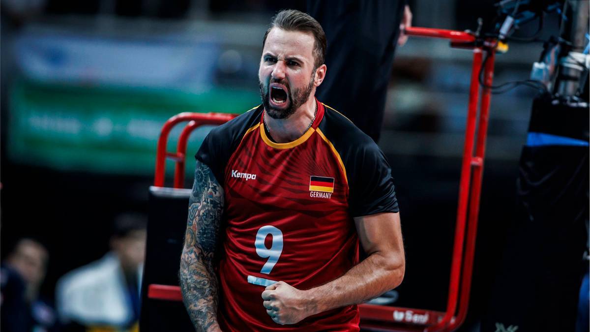 Mężczyzna w czerwonej koszulce z numerem 9, krzyczy z wysiłku podczas meczu siatkówki.