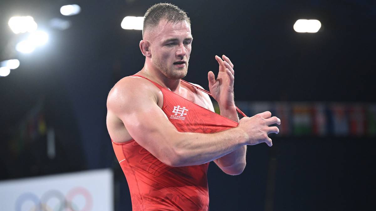 Zapaśnik w czerwonym stroju zdejmuje koszulkę po walce.