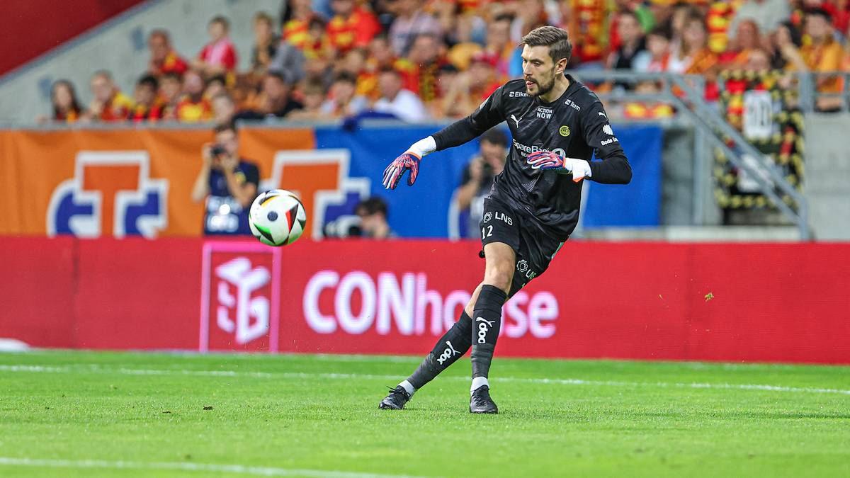 Bramkarz w akcji na boisku piłkarskim, kopiący piłkę.