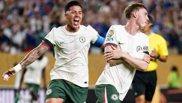 Dwóch piłkarzy w białych koszulkach z zielonymi spodenkami, cieszących się z bramki, podczas meczu.