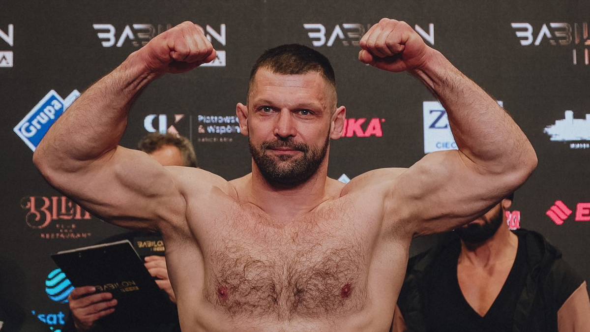 Mięśniowy mężczyzna prezentujący bicepsy na tle logotypów Babilon MMA.