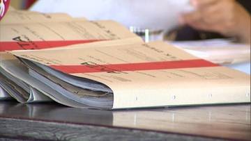 Stos papierowych dokument&oacute;w w teczkach, z czerwonym paskiem.