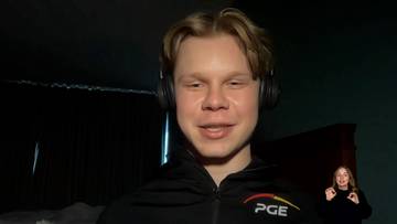 Młody mężczyzna z blond włosami i słuchawkami na uszach, ubrany w czarną bluzę z logo PGE, uśmiecha się do kamery. W rogu widać kobietę tłumaczącą język migowy.