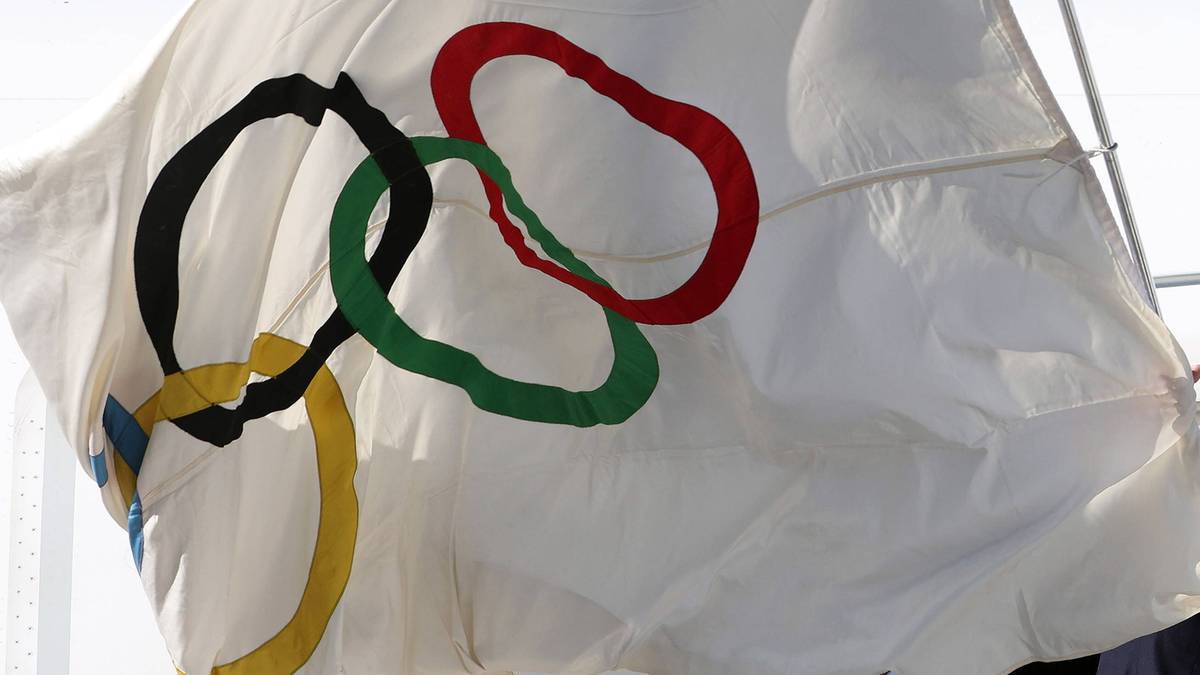 Biała flaga z kolorowymi kołami olimpijskimi falująca na wietrze.