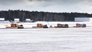 Pięć pomarańczowych pojazd&oacute;w odśnieżających na zaśnieżonym pasie lotniska.