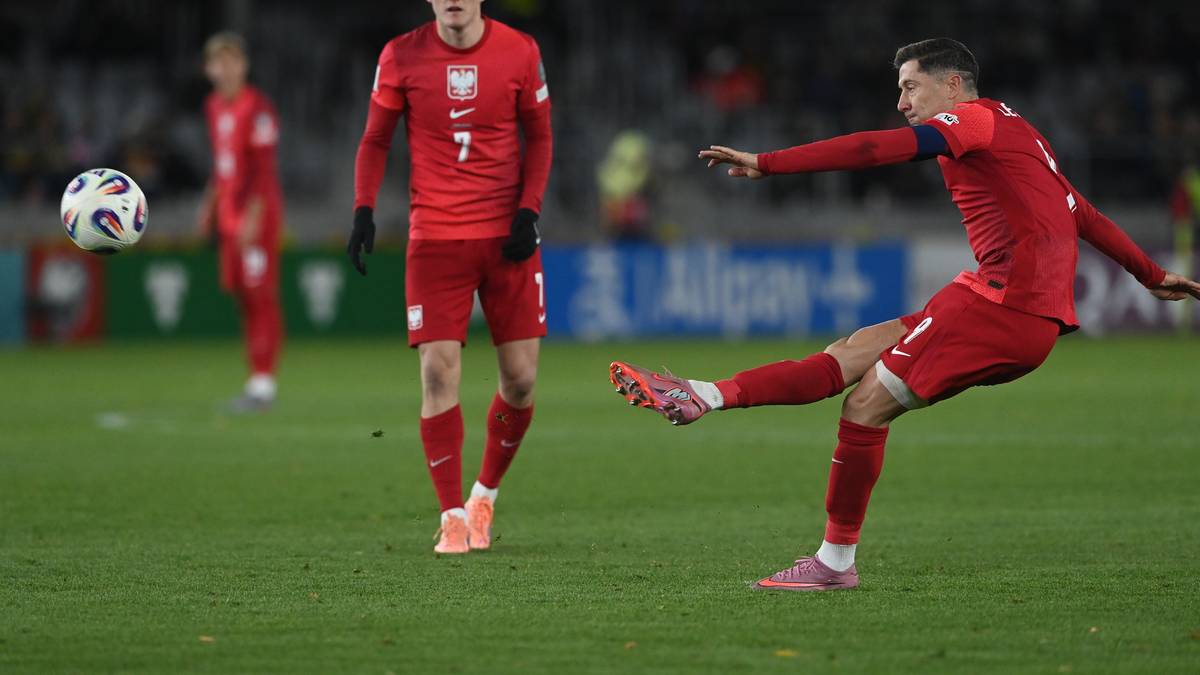 Piłkarz Robert Lewandowski w czerwonym stroju oddaje strzał do piłki. W tle widać innego zawodnika w czerwonej koszulce z numerem 7.