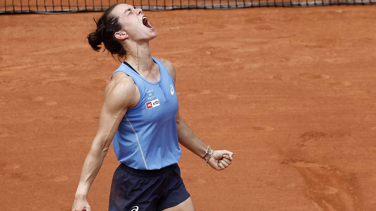 Tenisistka w niebieskim stroju krzyczy z radości na ceglanym korcie.