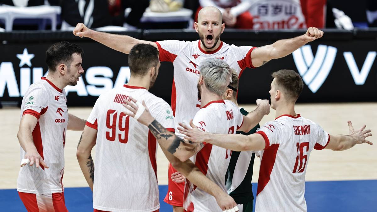 Pięciu polskich siatkarzy w białych koszulkach z czerwonymi elementami, świętujących sukces podczas meczu.
