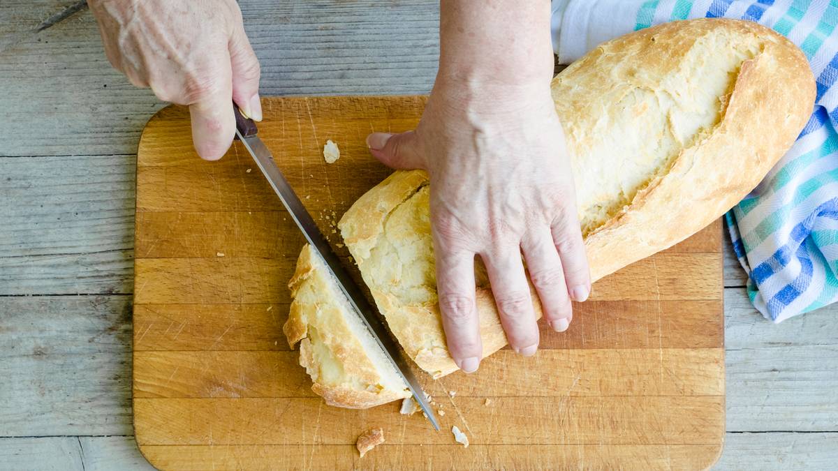 Dłonie kroją bagietkę na drewnianej desce