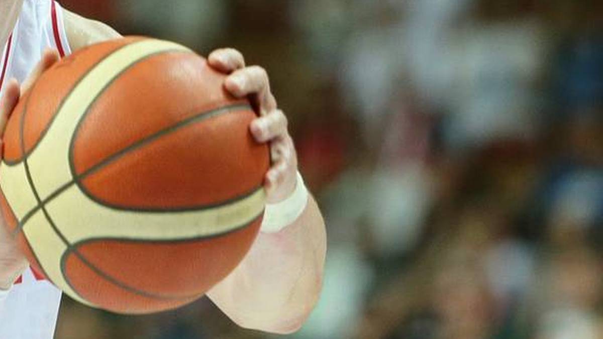 Koszykarz w białej koszulce z pomarańczową piłką w dłoniach, przygotowujący się do rzutu. W tle publiczność.