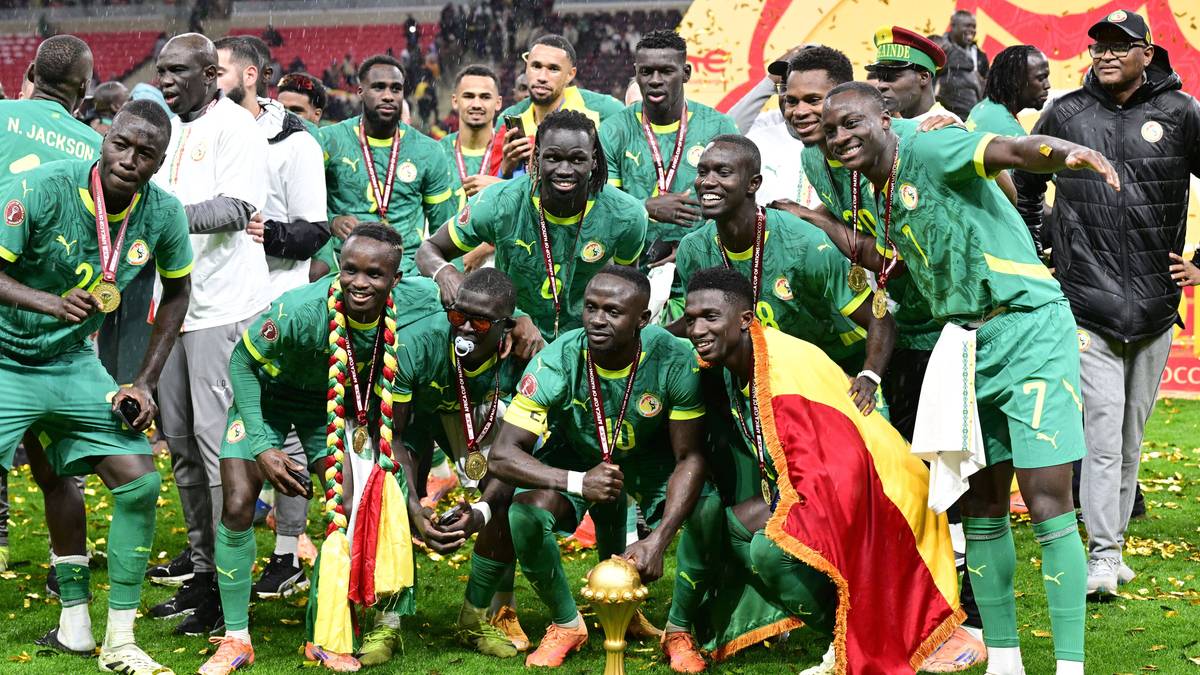 Piłkarze Senegalu w zielonych strojach pozują do zdjęcia z pucharem i medalami, świętując zwycięstwo w turnieju.