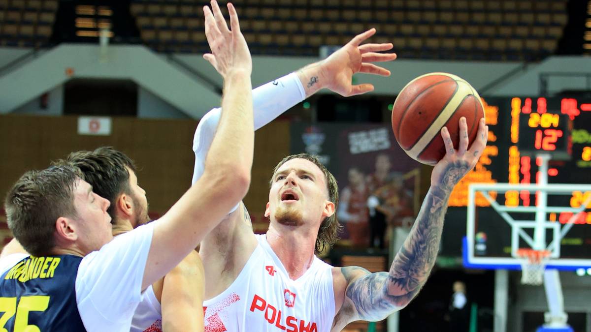 Czterech koszykarzy, trzech z nich w białych koszulkach z napisem "POLSKA", próbuje zdobyć piłkę. Jeden z zawodników jest na pierwszym planie, patrząc w górę na piłkę.