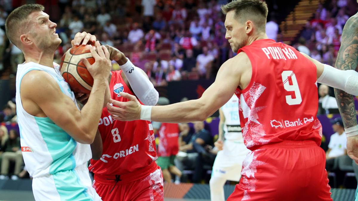 Dwóch zawodników koszykówki walczących o piłkę podczas meczu. Jeden w białej koszulce, drugi w czerwonej z numerem 9 na plecach.