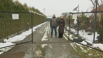 Para stoi przed otwartą bramą ogrodzenia.