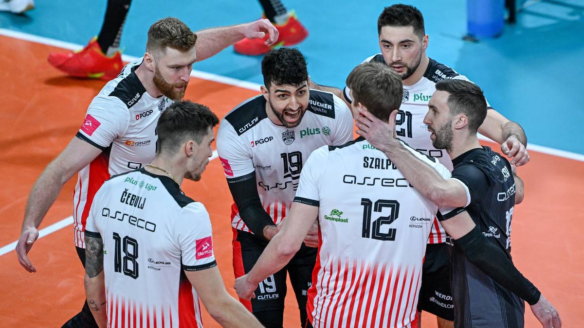 Sześciu siatkarzy w białych i czarnych strojach tworzy grupę na boisku siatkarskim.