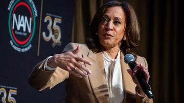 Kamala Harris przemawia do mikrofonu na tle logo.