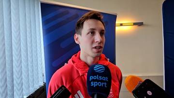 Mężczyzna w czerwonej bluzie z kapturem, ubrany w białą koszulkę z nadrukiem, udziela wywiadu przed mikrofonem z logo "Polsat Sport".