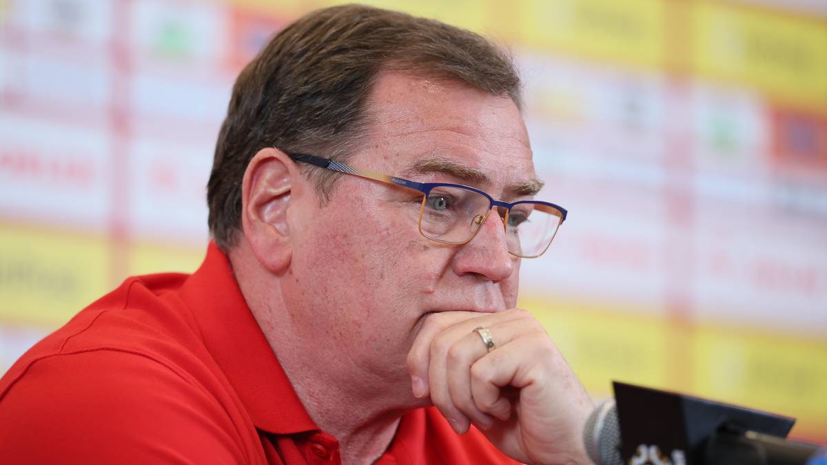 Mężczyzna w okularach i czerwonej koszuli zamyślony podczas konferencji prasowej