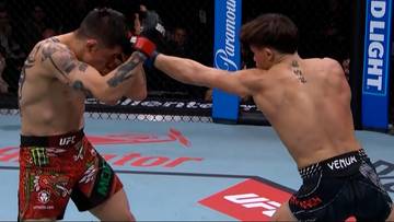 Dw&oacute;ch zawodnik&oacute;w MMA walczy w oktagonie, jeden wykonuje unik, drugi wyprowadza cios.