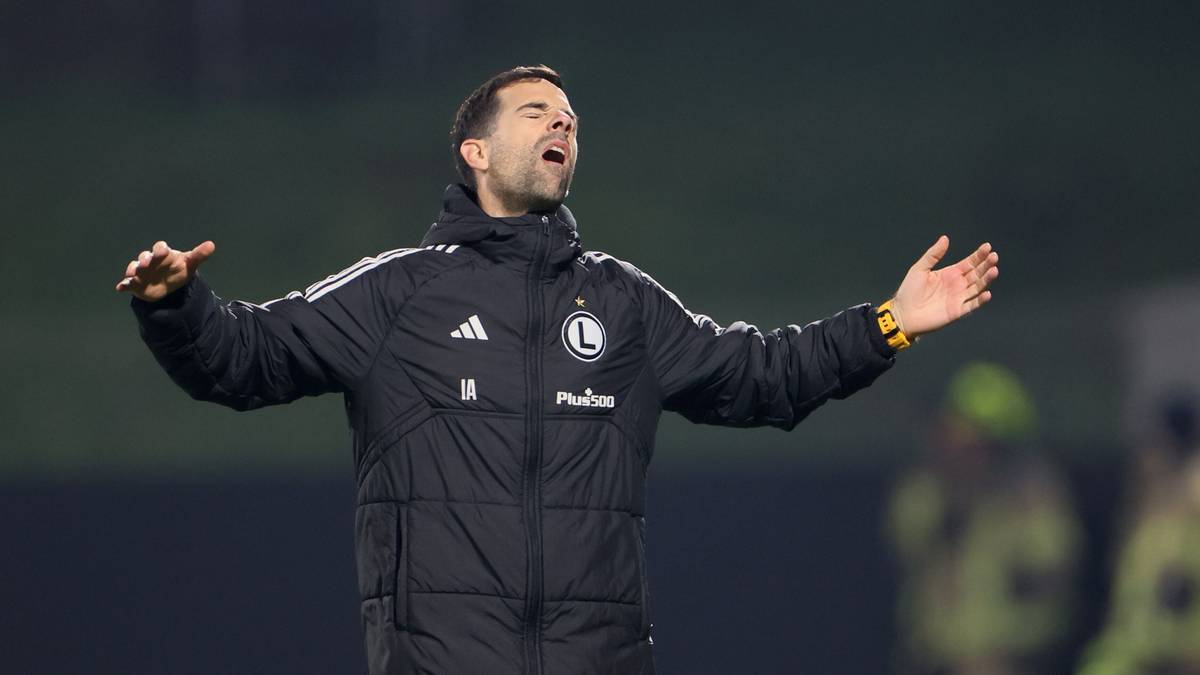 Kosta Runjaić, tymczasowy trener Legii Warszawa, w kurtce klubowej, z otwartymi ramionami na boisku.