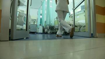 Osoba w białym stroju medycznym wchodzi do sali szpitalnej.