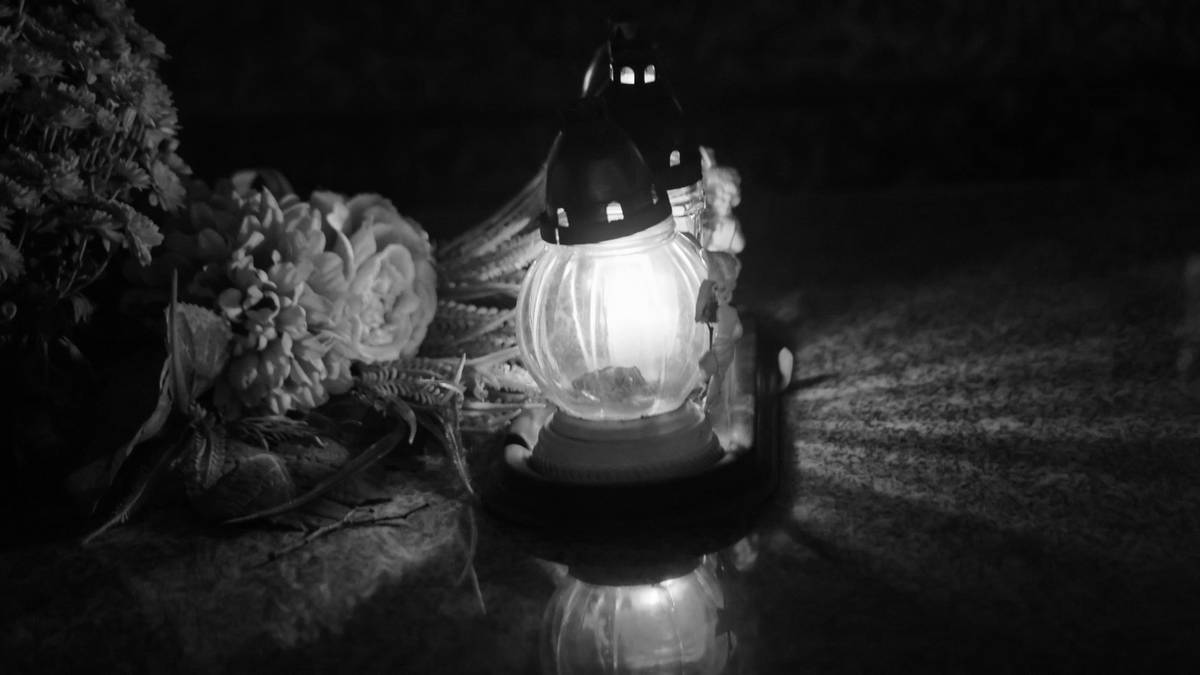 Zapalone znicz obok wiązanki kwiat&oacute;w w ciemności.