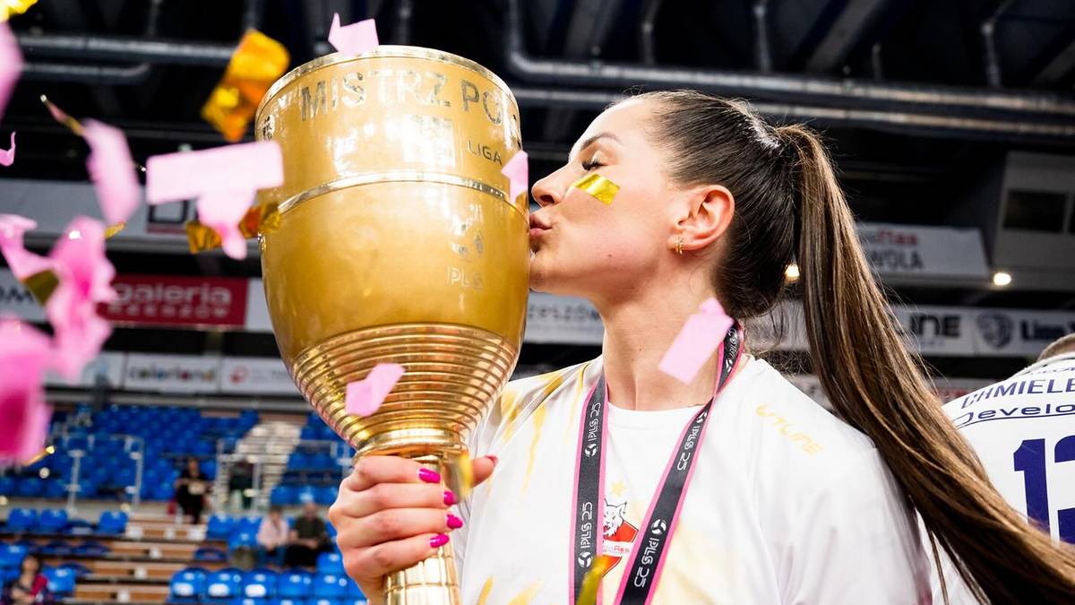 Uśmiechnięta siatkarka całuje złoty puchar, w tle konfetti i trybuny.