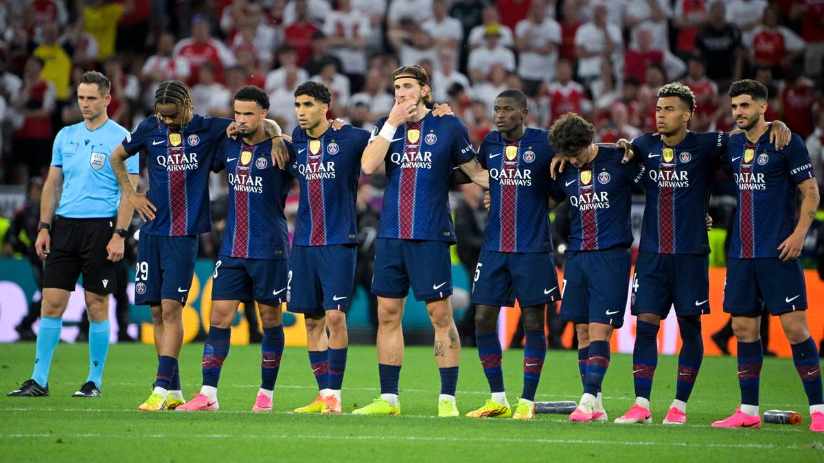 Drużyna piłkarska Paris Saint-Germain w niebieskich strojach stoi w rzędzie na boisku.