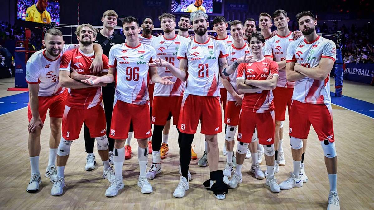 Drużyna siatkarzy Polski w białych koszulkach i czerwonych spodenkach, pozująca do zdjęcia na boisku.