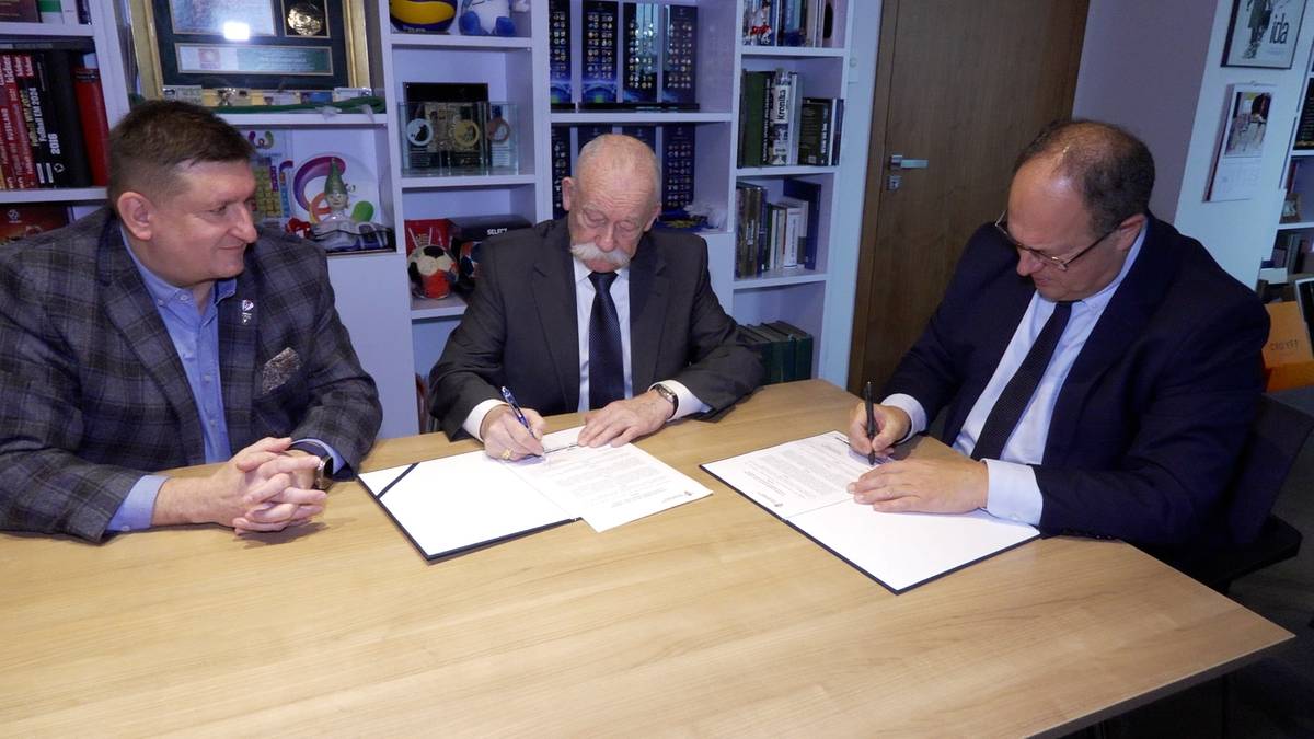 Trzech mężczyzn w garniturach przy stole podpisuje dokumenty.